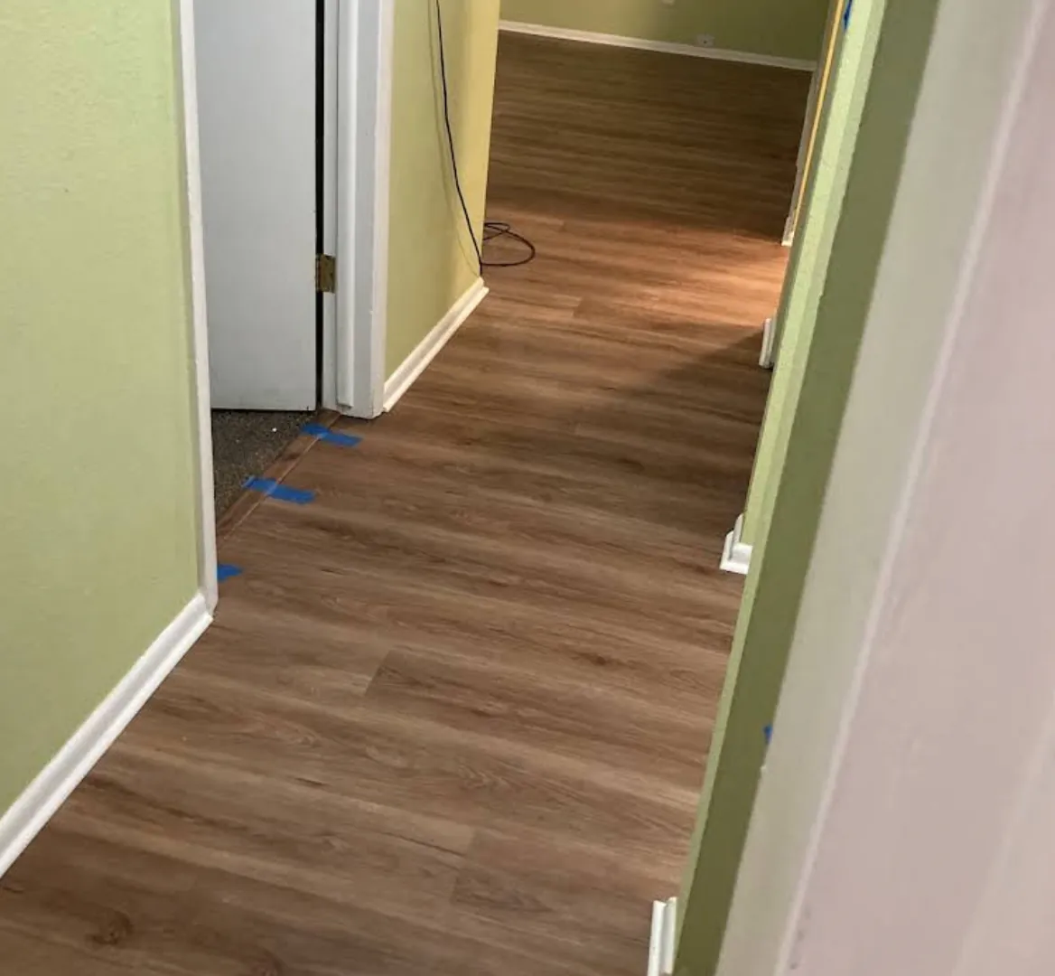 Hallway with newly installed brown plank flooring leading to a doorway